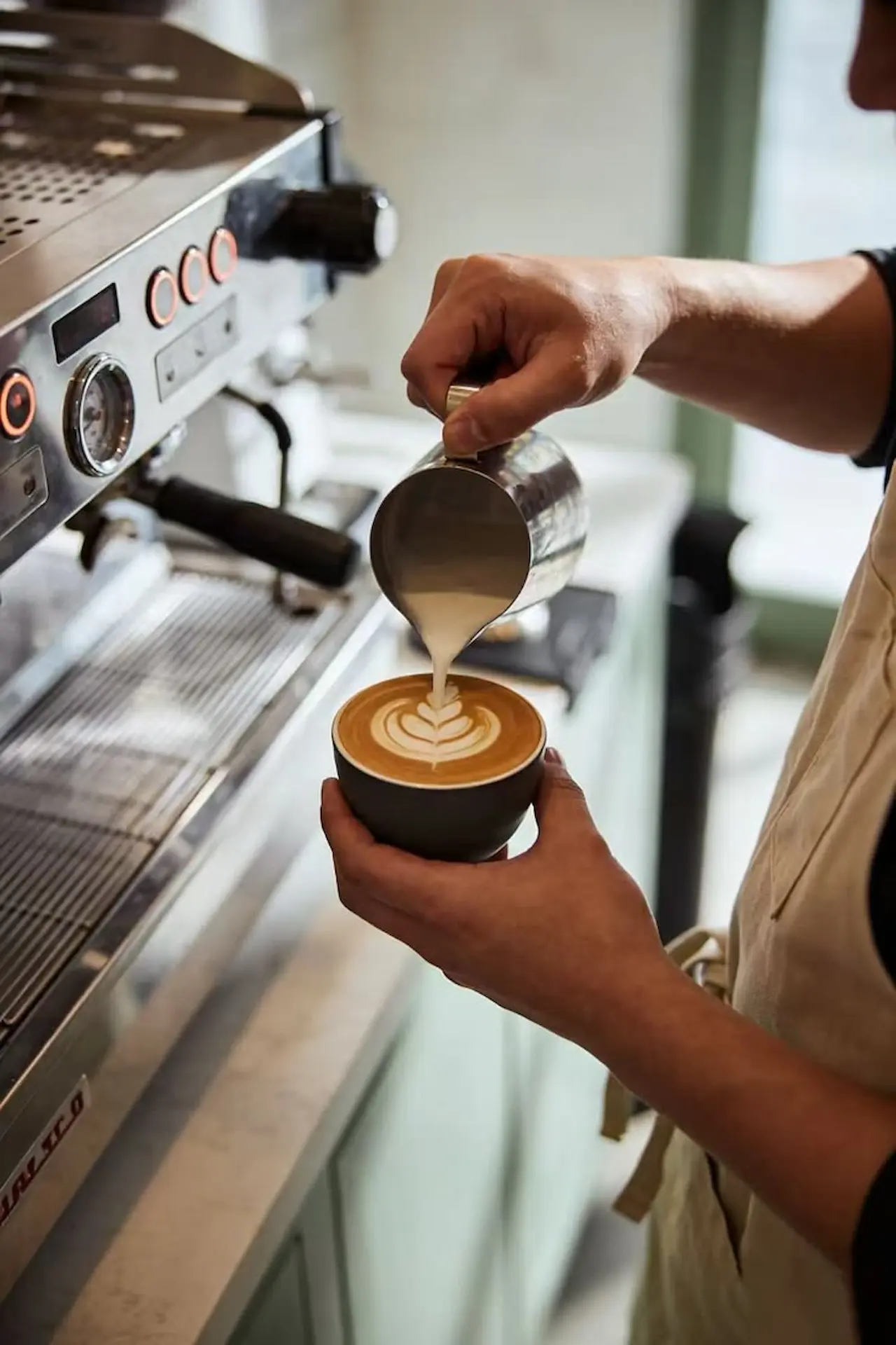 Barista Time Coffee sedang menuang susu membentuk latte art di atas cangkir kopi